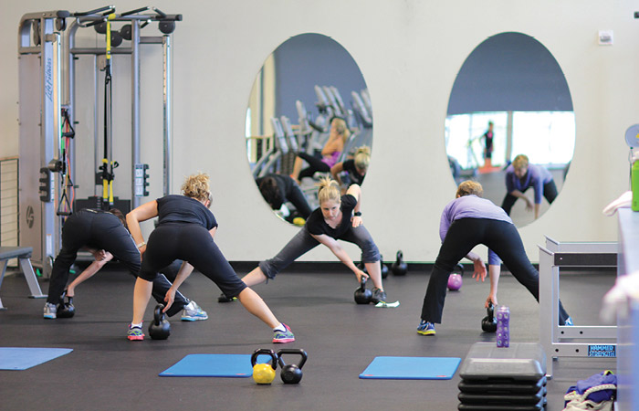 Breanne-small-group_0075 Group fitness class lunges to grab kettlebells.