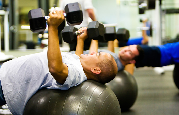 Power Circuit Group Fitness Class Men on bosu ball holding dumbells in chest fly position in Power Circuit HIIT Class