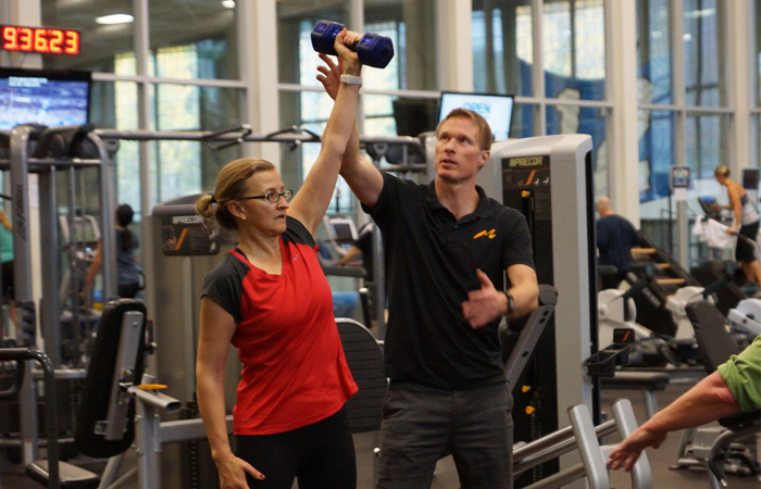 Instructor guides woman as she holds a dumbbell up.