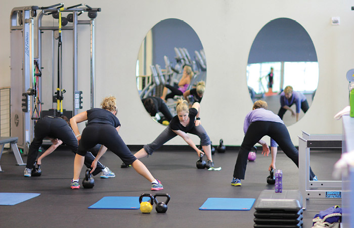 Group fitness class lunges to grab kettlebells.