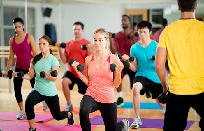 Group of people in burn class with dumbells in a curl position while lunging