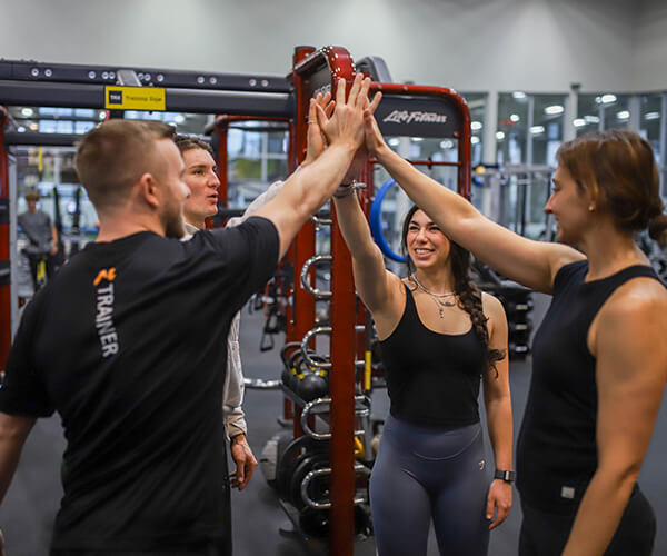 A group of people standing in a weight room at Magnuson Athletic Club high-five each other