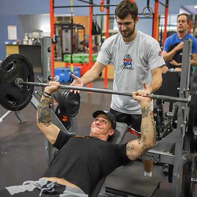 A man helps another with a barbell chest press exercise during Strength Training class at Magnuson Athletic Club in Seattle