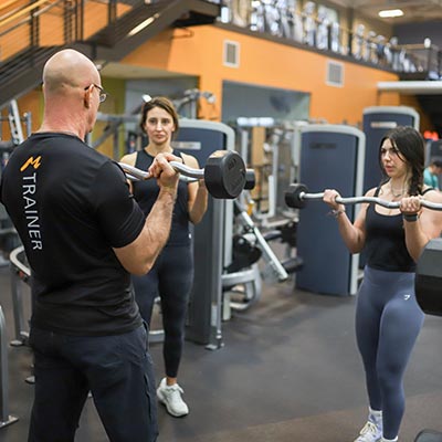 A trainer demonstrates a barbell exercise to two women during Strength Training class at Magnuson Athletic Club in Seattle